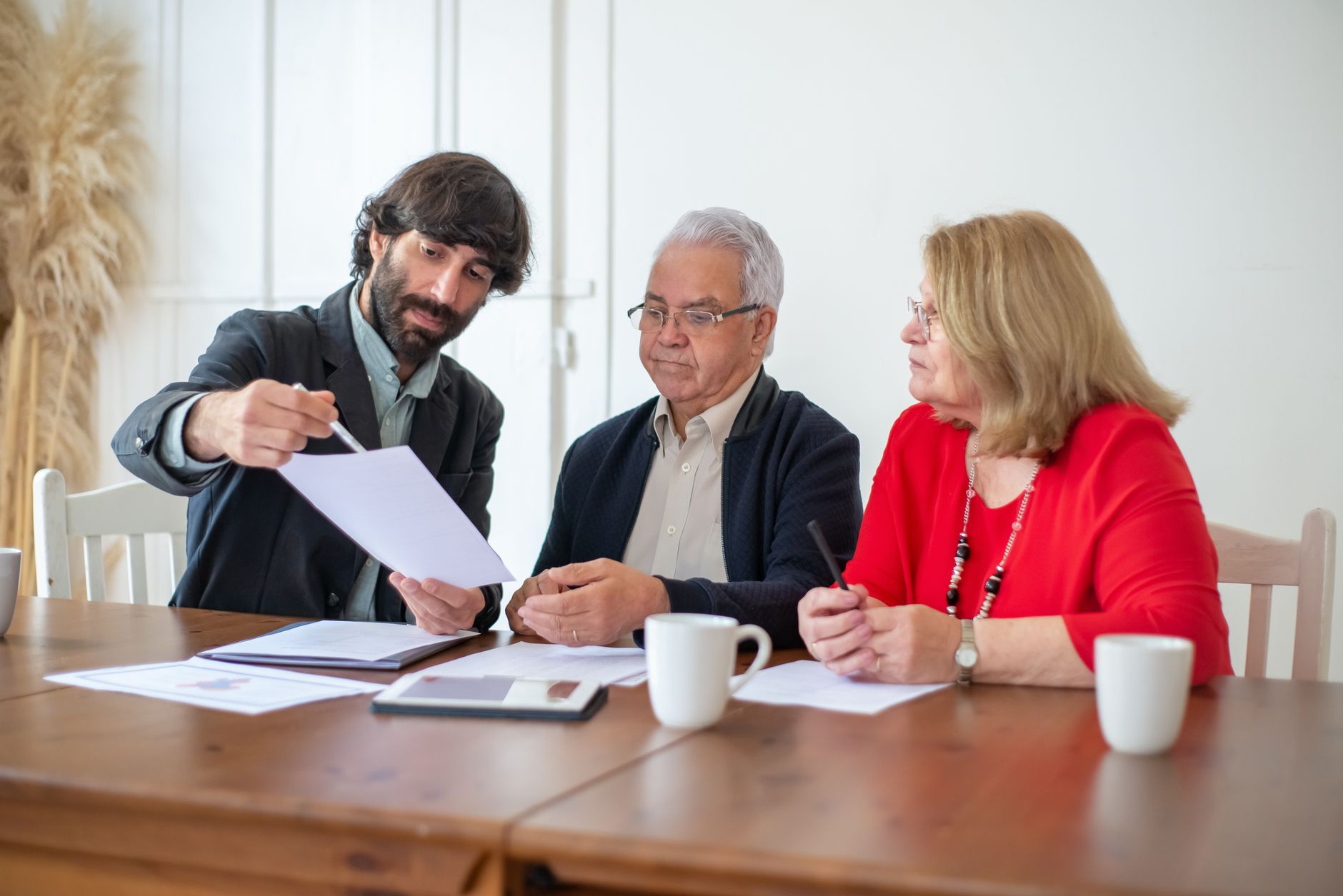 An adviser pointing to a printed page for an older couple at a wooden table